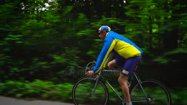 Homem de meia-idade está montando uma bicicleta de estrada ao longo de uma estrada da floresta, câmera lenta — Vídeo de Stock