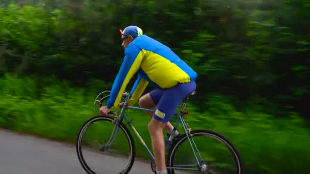 Чоловік середнього віку їде на шосейному велосипеді вздовж лісової дороги — стокове відео