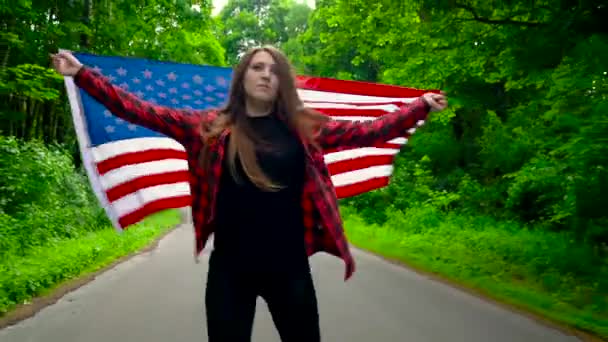 Jovem adolescente com bandeira dos EUA patina na floresta e segura a mão de outra pessoa — Vídeo de Stock