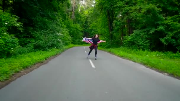Молодая девушка-подросток с флагом США катается на роликах по лесу и держит за руку другого человека — стоковое видео