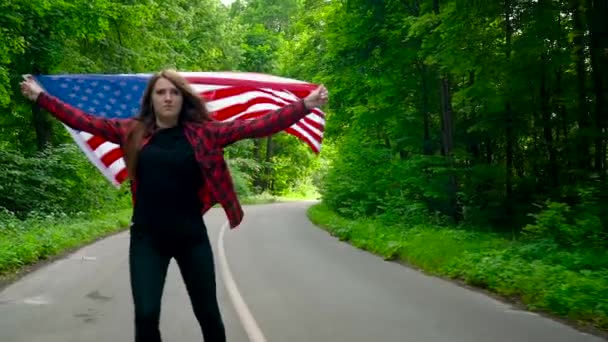 Jovem adolescente acenando uma bandeira dos EUA está patinando através da floresta. Movimento lento — Vídeo de Stock