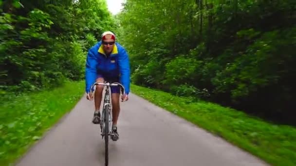 Чоловік середнього віку їде на шосейному велосипеді вздовж лісової дороги — стокове відео