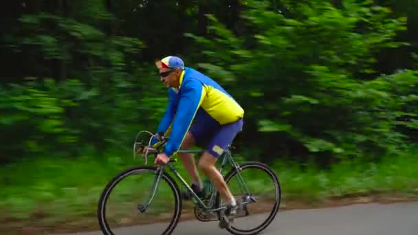Hombre de mediana edad está montando una bicicleta de carretera a lo largo de un camino forestal, cámara lenta — Vídeos de Stock