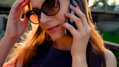 Kadın güneş gözlüğü smartphone üzerinde söz ederken kadar günbatımı, yakın sokakta yürüyen, yakın çekim