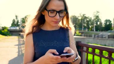 Gün batımında sokakta yürürken bir smartphone kadın gözlük kullanır