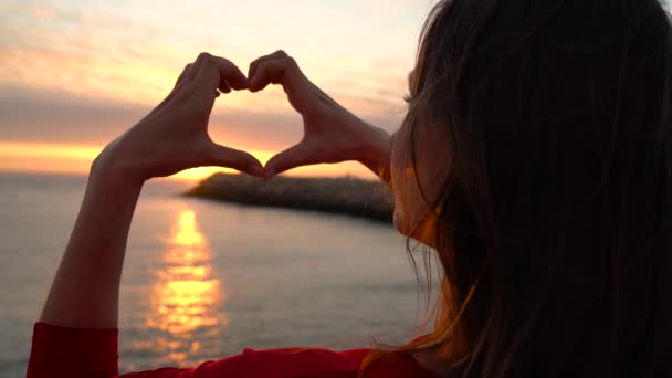 女人做心脏符号用她的双手在日落海滩上 — 图库视频影像