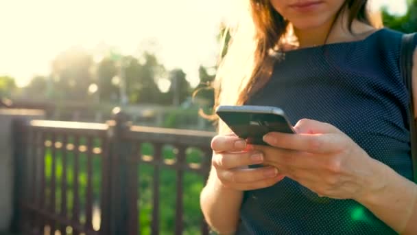 Femme utilise un smartphone tout en marchant dans la rue, au coucher du soleil une vue arrière — Video