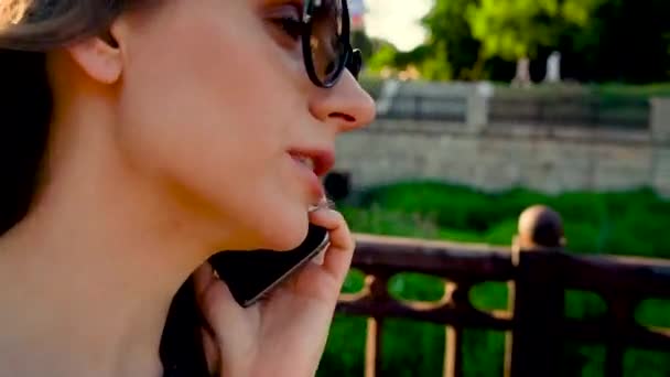 Nő beszél a smartphone, míg az utcán a naplemente, zár megjelöl, közeli napszemüveg — Stock videók