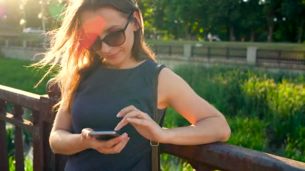 Vrouw in met behulp van een smartphone buitenshuis bij zonsondergang zonnebril — Stockvideo