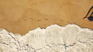 Üstten Görünüm yalınayak ıslak kum okyanus plaj boyunca yürüyen bir kadın. Kumun üzerinde çalışan dalga uzakta ayak yıkama