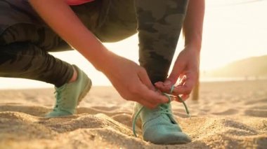 Koşu ayakkabıları - kadın ayakkabı bağcıklarımı kumsalda gün batımında bağlıyor.