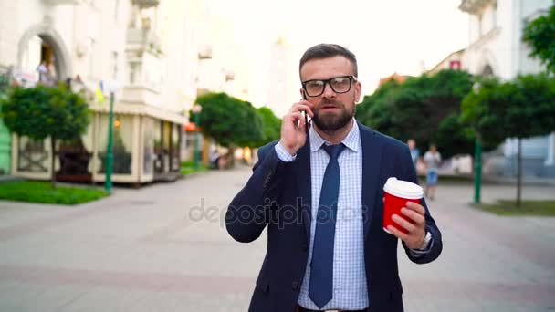 Man talking on smartphone and drinking coffee walking down the street. Slow motion — Stock Video