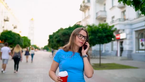 Femme parlant sur le smartphone et buvant du café marchant dans la rue — Video