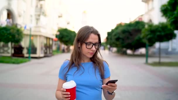 Femme parlant sur le smartphone et buvant du café marchant dans la rue — Video