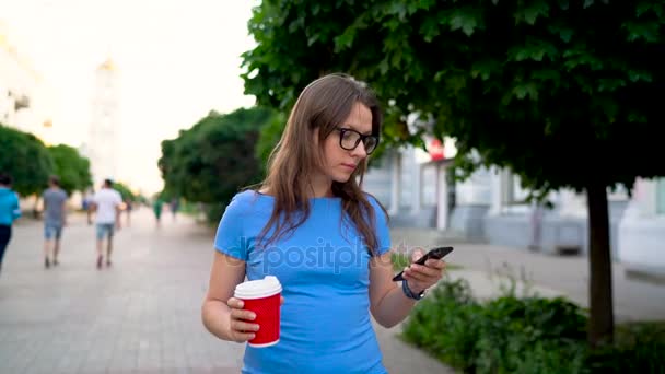 Женщина разговаривает по смартфону и пьет кофе, идя по улице. Медленное движение — стоковое видео