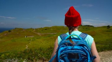 Kadın bir sırt çantası ile pitoresk bir engebeli arazide okyanusa doğru gidiyor.