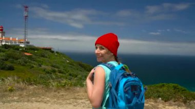 Kadın bir sırt çantası ile pitoresk bir engebeli arazide okyanus deniz fenerinde gider