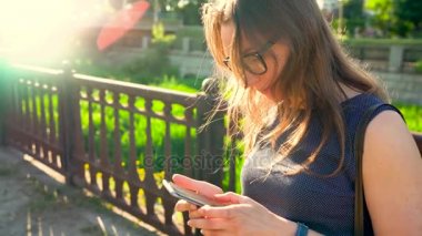 Kadın bir akıllı telefon açık havada günbatımında kullanarak güneş gözlüğü