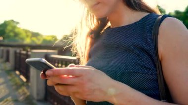 Kadın bir akıllı telefon açık havada günbatımında kullanarak güneş gözlüğü