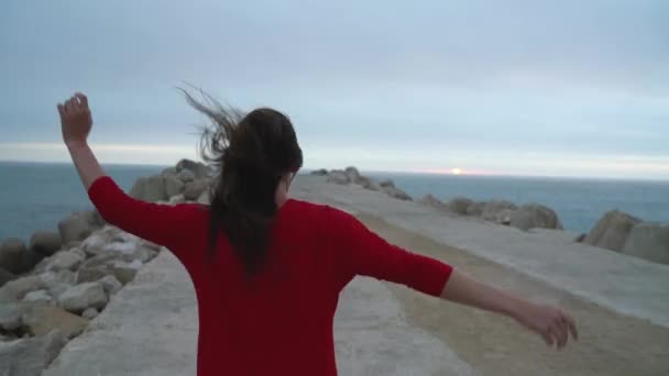 Жінка в червоній сукні біжить до маяка на узбережжі океану — стокове відео