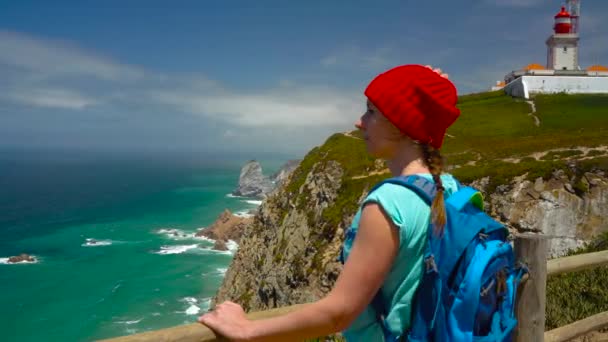 Mujer con una mochila disfruta de una vista de la costa del océano cerca del faro — Vídeo de stock