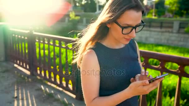 Γυναίκα χρησιμοποιεί ένα smartphone, ενώ το περπάτημα στο δρόμο, στο ηλιοβασίλεμα — Αρχείο Βίντεο