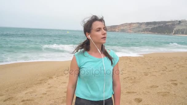 Mujer en la playa escuchando música en auriculares desde un teléfono inteligente. Nazare, Portugal. Movimiento lento — Vídeos de Stock