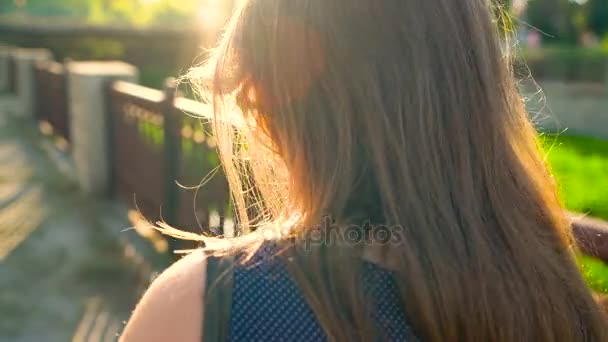 Woman uses a smartphone while walking down the street, at sunset - a back view — Stock Video