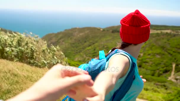 3 in 1 video. Woman with a backpack behind her back gives her hand to her companion, standing on top of a hill on the ocean shore — Stock Video