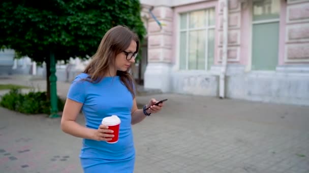 Mujer hablando en el teléfono inteligente y tomando café caminando por la calle. Movimiento lento — Vídeos de Stock