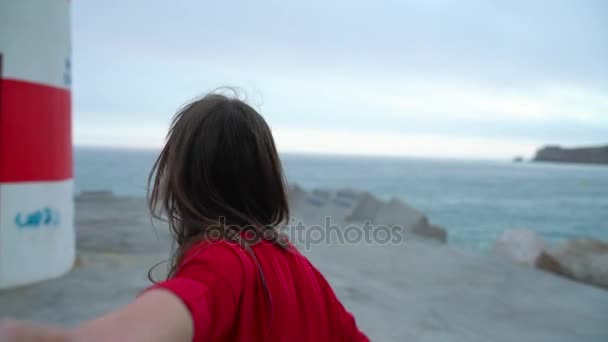 Za mnou - šťastná mladá žena v červených šatech tahání kluci ruka - ruku v ruce chůzi k majáku na pláži při západu slunce, pomalý pohyb — Stock video
