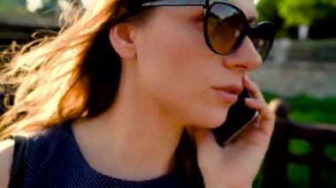 Kadın güneş gözlüğü smartphone üzerinde söz ederken kadar günbatımı, yakın sokakta yürüyen, yakın çekim