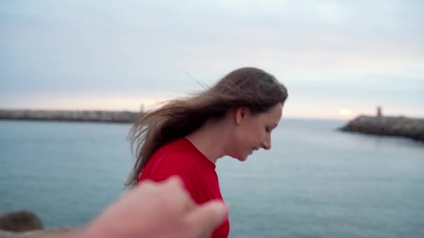 Seguimi - giovane donna felice in abito rosso tirando ragazzi mano nella mano - camminando verso il faro sulla spiaggia al tramonto . — Video Stock