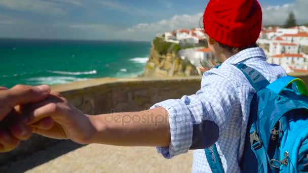 Sígueme - mujer joven feliz con un sombrero rojo y con una mochila detrás de su espalda tirando de chicos mano en Azenhas do Mar, Portugal. Caminando de la mano a la costa del océano — Vídeo de stock