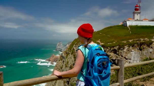 Mujer con una mochila disfruta de una vista de la costa del océano cerca del faro — Vídeo de stock