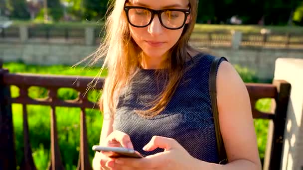 Γυναίκα σε γυαλιά ηλίου χρησιμοποιώντας ένα smartphone σε εξωτερικούς χώρους στο ηλιοβασίλεμα — Αρχείο Βίντεο