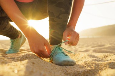 Koşu ayakkabıları - kadın ayakkabı bağcıklarımı kumsalda gün batımında bağlıyor.
