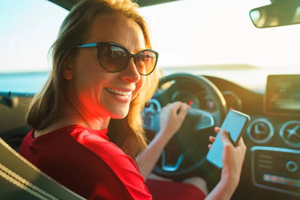 Mujer feliz utiliza un teléfono inteligente mientras conduce un coche — Foto de Stock
