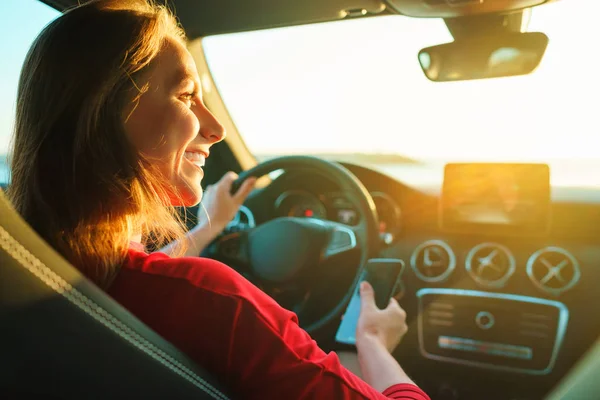 Mulher feliz usa um smartphone enquanto dirige um carro — Fotografia de Stock