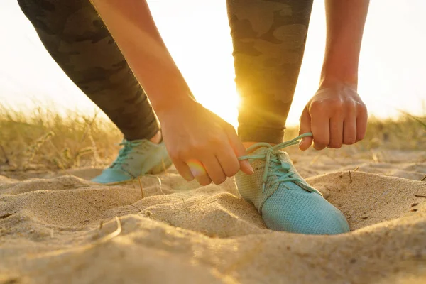 Sepatu lari wanita mengikat tali sepatu di pantai berpasir saat matahari terbenam — Stok Foto