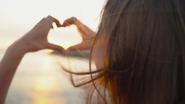 Frau macht Herzsymbol mit ihren Händen während des Sonnenuntergangs am Strand — Stockvideo