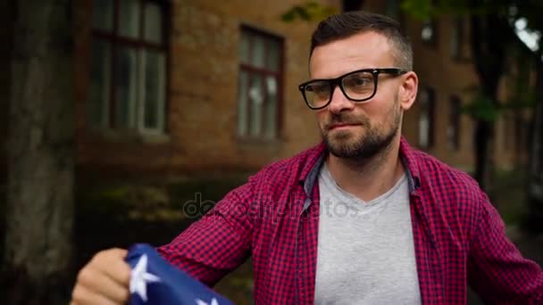 Homem acenando uma bandeira dos EUA enquanto caminhava ao longo da rua o conceito de Dia da Independência dos EUA. Movimento lento — Vídeo de Stock