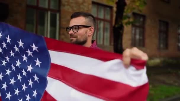 El hombre ondeando una bandera de Estados Unidos mientras camina por la calle - el concepto del Día de la Independencia de Estados Unidos — Vídeos de Stock