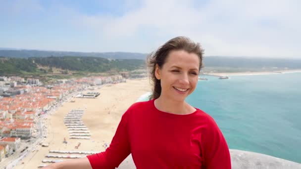 Žena v červených šatech relaxační na vršku nad městem Nazaret, Portugalsko — Stock video