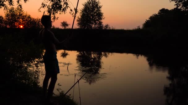 Silueta de un pescador en la orilla del río al atardecer — Vídeos de Stock