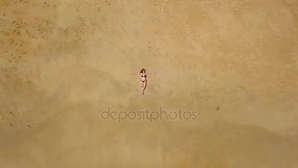 Antenn skott av en kvinna i en bikini som ligger på en sandstrand och vågor tvätta hennes fötter — Stockvideo