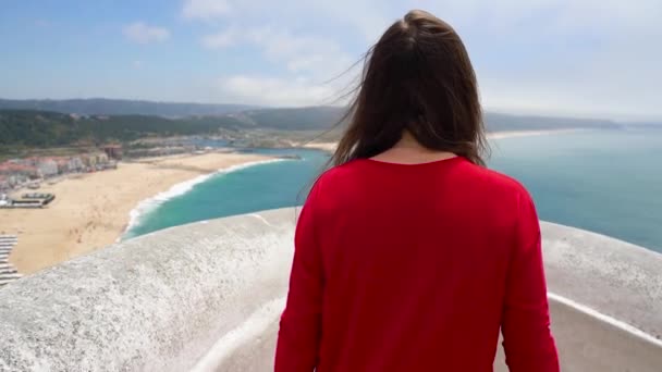 Piros ruhás nő élvezi a kilátás nyílik az óceán partja közelében Nazare, Portugália. Lassú mozgás — Stock videók