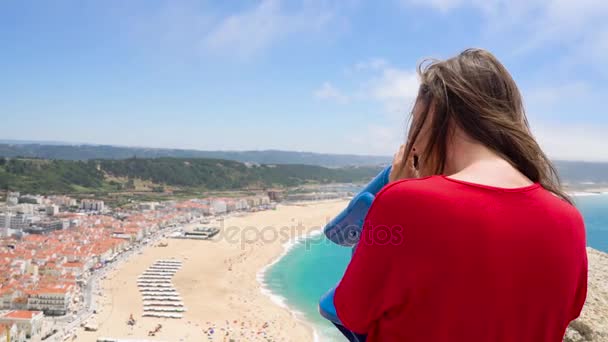 Turista femenina usando binoculares pagados con monedas en alta colina y mirando el paisaje urbano de Nazaret, Portugal — Vídeo de stock