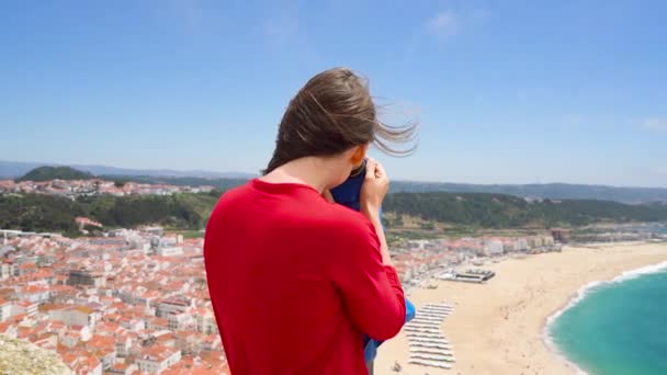 Turista femminile che usa un binocolo a gettoni in alta collina e guarda il paesaggio urbano di Nazareth, Portogallo, al rallentatore — Video Stock