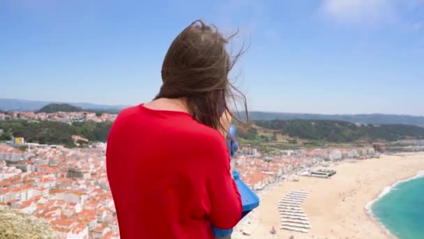 Vrouwelijke toeristische met munt betaald verrekijkers op hoge heuvel en kijken naar stadsgezicht van Nazareth, Portugal — Stockvideo